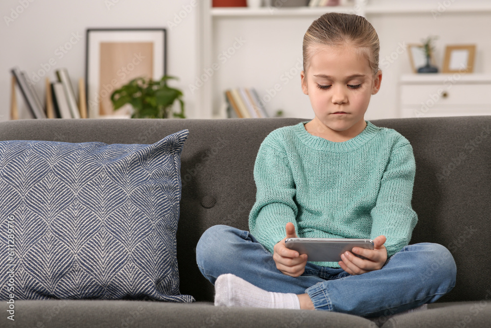 Obraz premium Little girl using smartphone on sofa at home. Internet addiction
