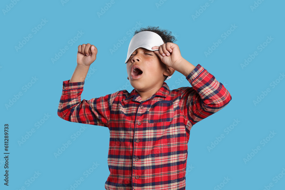 Boy with sleep mask yawning and stretching on light blue background. Insomnia problem Boy with sleep mask yawning and stretching on light blue background. Insomnia problem