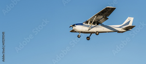 Small white plane with blue stripes of a cessna propeller flying from side view point of view in a clear blue cloudless sky before landing at Sabadell airport. photo