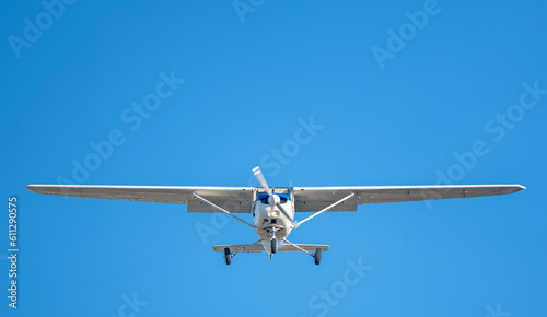 Small white plane with blue stripes of a cessna propeller flying in a clear sky before landing on Sabadell Airport
