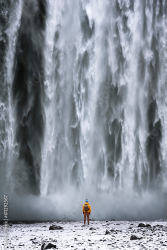 A tourist, adorned in a vibrant yellow raincoat, strolls gracefully from the majestic Skogafoss waterfall in Iceland. The enchanting cascade is located along the Skoga River