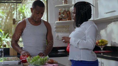 brazilian black woman drinking coffee in the kitchen and talking to hier boyfriend while he cuts vegetables for his valentine's day lunch photo