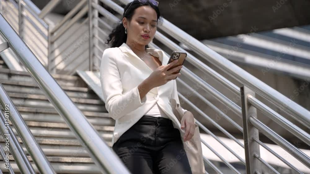 Professional Thai young businesswoman walking on stairs with her smartphone Professional Thai young businesswoman walking on stairs with her smartphone