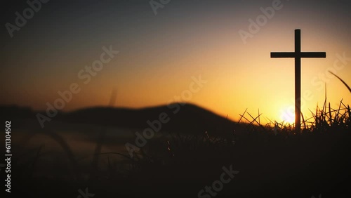 The holy cross of Jesus Christ on the grass with the strong light of the sunset sky symbolizes death and resurrection love.
