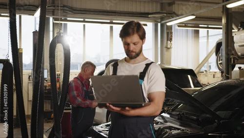Engineer with laptop makes computer diagnostics of the car engine in auto-service. Vehicle wiring inspection. Car service, repair, maintenance and people concept. Engineer makes computer diagnostics.