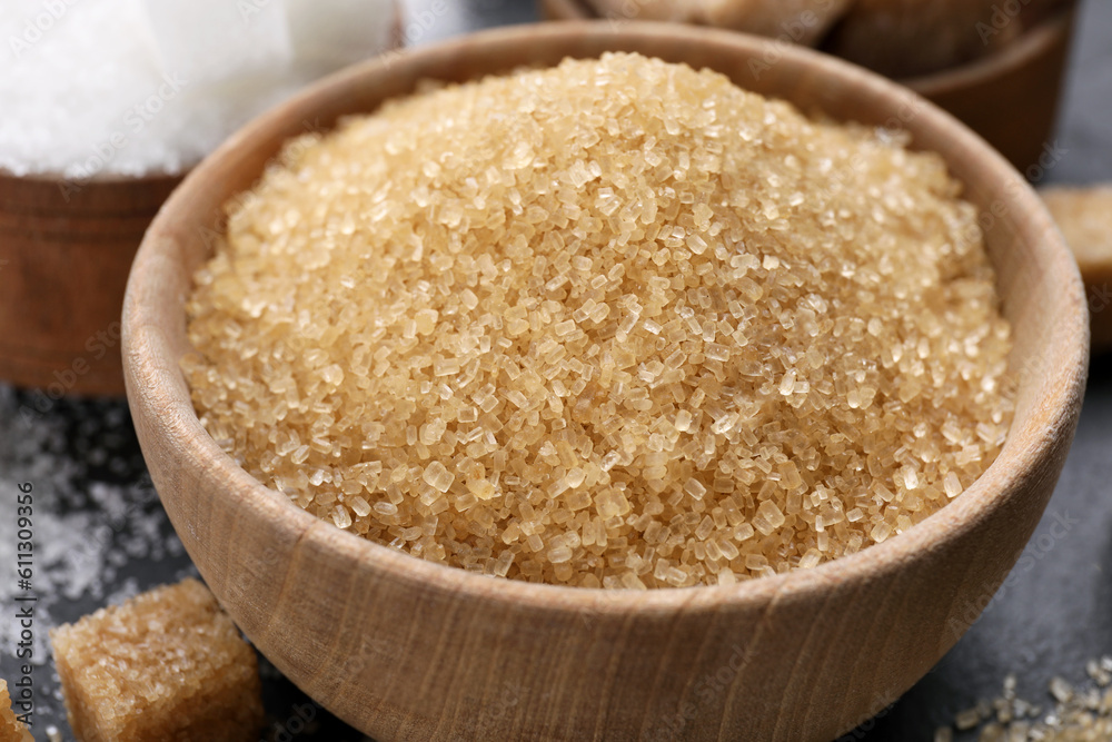 Brown granulated sugar in wooden bowl on black table, closeup Brown granulated sugar in wooden bowl on black table, closeup