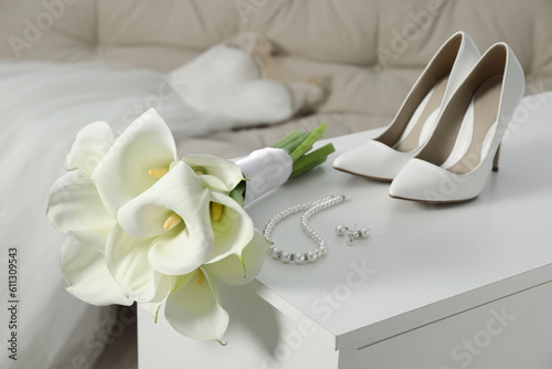 Beautiful calla lily flowers tied with ribbon  shoes and jewelry on white chest of drawers indoors