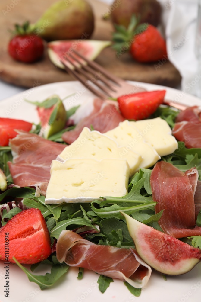 Tasty salad with brie cheese, prosciutto, strawberries and figs on white plate, closeup