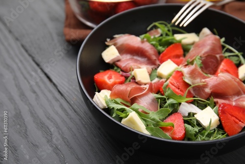 Tasty salad with brie cheese, prosciutto and strawberries on grey wooden table, closeup. Space for text