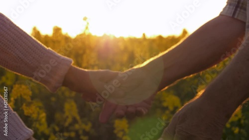 Close up of arms parting elderly people. Touching gesture separation of couple old spouses. They hold each other hands until last they don't want to let go. Outdoor rural field against sunset rays photo