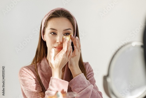 Portrait of brunette woman in rose pajamas applying a face patches