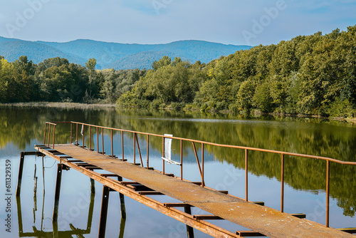 Long rusty walkway jetty reaches out to freshwater lake in hilly landscape