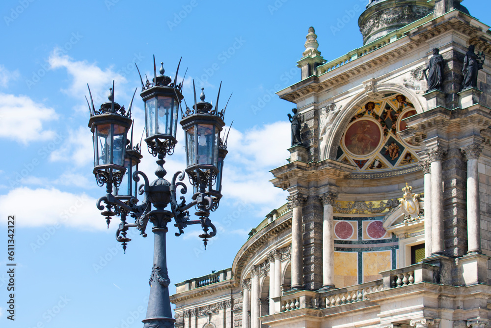 Facade of ancient architectural building with beige walls, statues, decorative elements and lantern. Historical architecture. Old town. Opera House. Sunny day, blue sky. Dresden, Germany, May 2023 