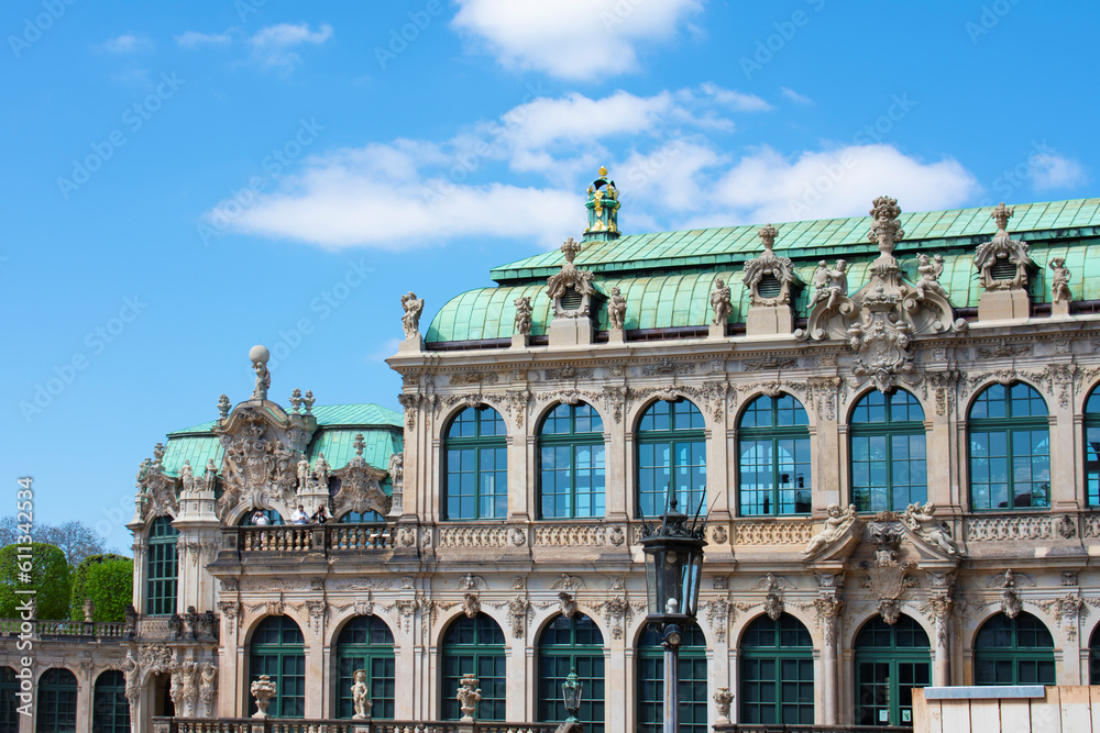 Obraz premium Facade of ancient building with beige walls, statues, decorative elements, semicircular windows and green roof. Historical architecture in the baroque style. Dresden, Art Gallery, Germany, May 2023 