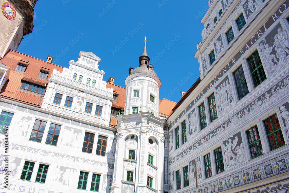 View of ancient building with white walls and grey graphic paintings, with towers and spires, windows and red roof. Old architecture, palace. Sunny day with blue sky. Dresden, Germany, May 2023.