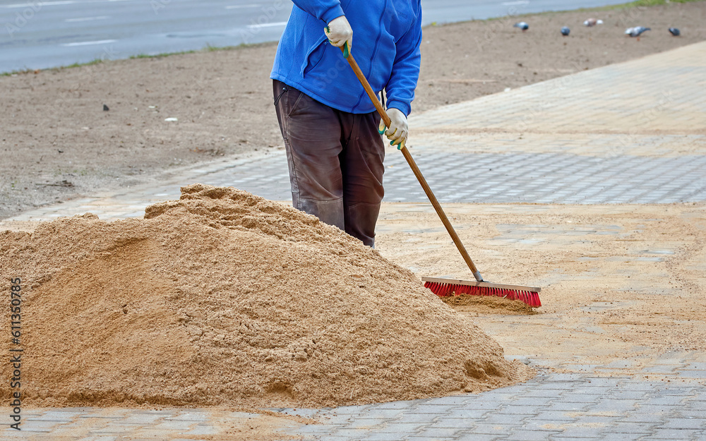 Pile of sand lies on new sidewalk, man seal seams between paving slabs