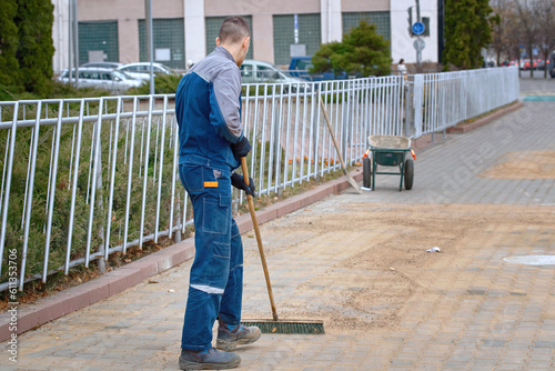 Worker with stiff brush grout and point paving slabs, paving industry. Worker fill the gaps with sand between paving slabs. Seal seams between paving slabs. Worker rubs the sand between tile.