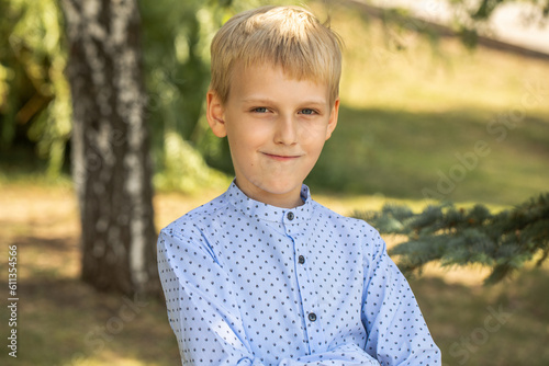 Portrait of a little boy in a blue shirt posing in a summer park