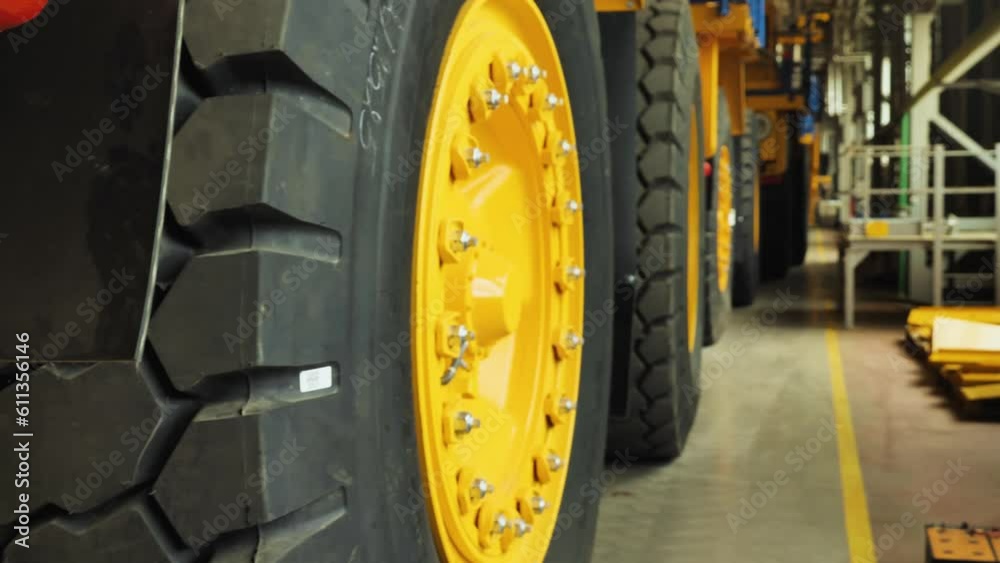 Big wheels of trucks. Mine dump trucks assembly line. Ready trucks stand in a row in the production hall. Production of big yellow mining trucks BelAZ