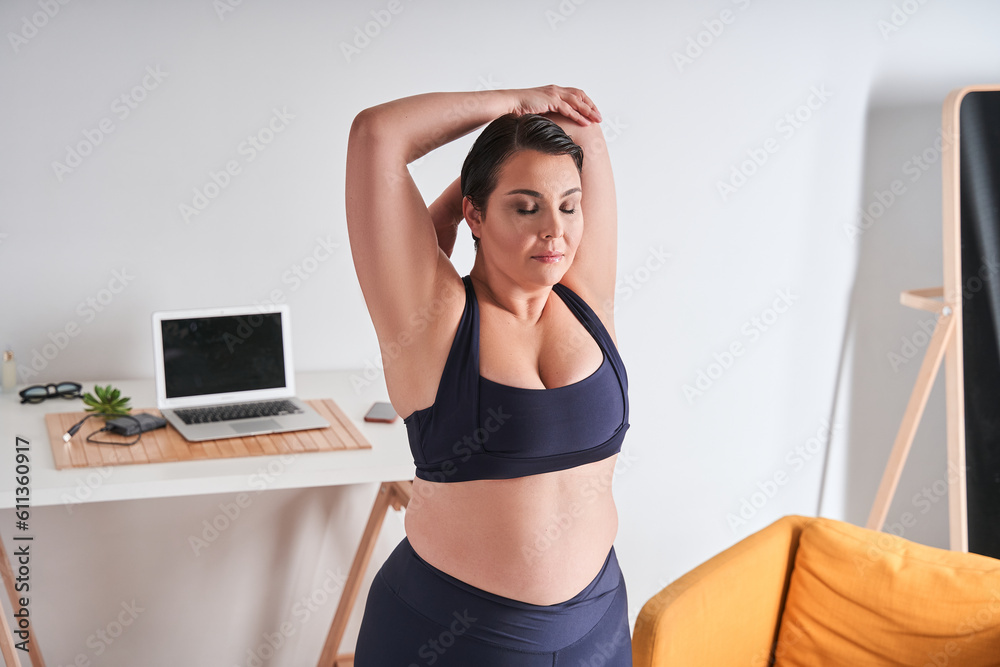 Serious plus size woman in sporty clothes stretching hands while doing sports Serious plus size woman in sporty clothes stretching hands while doing sports
