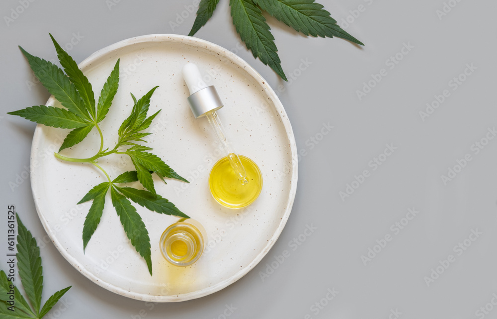 Dropper bottle and pipette near green cannabis leaves on grey table. Cosmetic Mockup Dropper bottle and pipette near green cannabis leaves on grey table. Cosmetic Mockup
