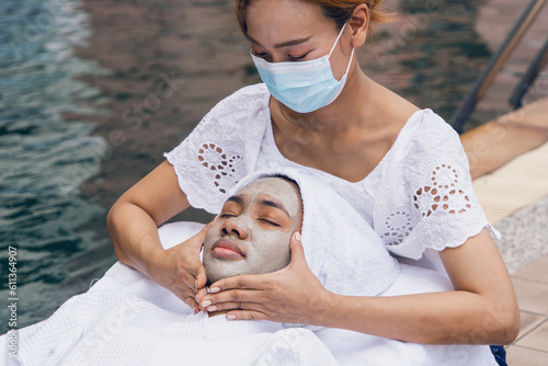 African American woman creamy facial mask and use cucumber slices to cover the eyes near swimming pool at resort and spa.Wellness and beauty health concept photo