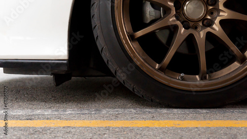 Down view of gold alloy wheels of sports cars. Car white color stop in the parking lot with yellow line on asphalt road.