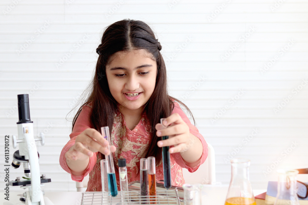 Cute Indian school girl in India traditional dress costume doing science experiments in laboratory, young scientist kid with microscope and lab equipment learning biologics and chemistry in classroom. Cute Indian school girl in India traditional dress costume doing science experiments in laboratory, young scientist kid with microscope and lab equipment learning biologics and chemistry in classroom.