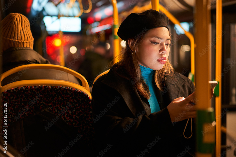 Teen asian woman in black hat messaging on smartphone at the bus