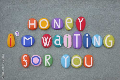 Honey, I am waiting for you, love message composed with multi colored stone letters over green sand