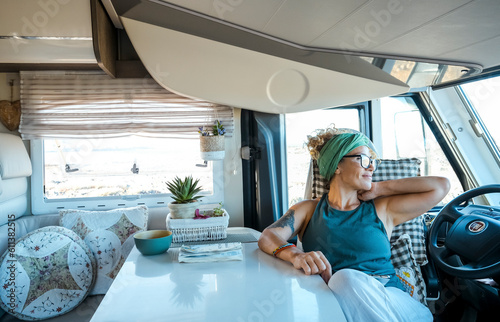 One young traveler woman enjoy time and relax inside modern camper van . Vanlifer smile sitting on driver seat looking outside at destination. Summer road trip vacation adventure female- Trendy life