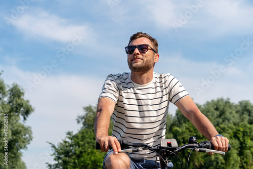 Adult man wearing sunglasses rides on his bicycle on the weekend in summer.