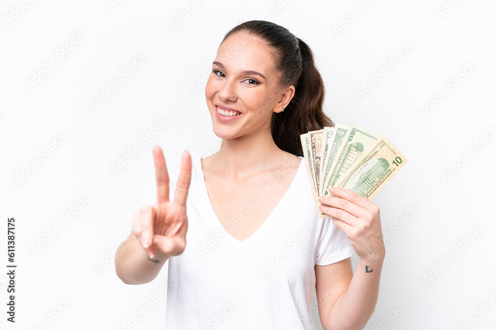 Young caucasian woman taking a lot of money isolated on white background smiling and showing victory sign Young caucasian woman taking a lot of money isolated on white background smiling and showing victory sign