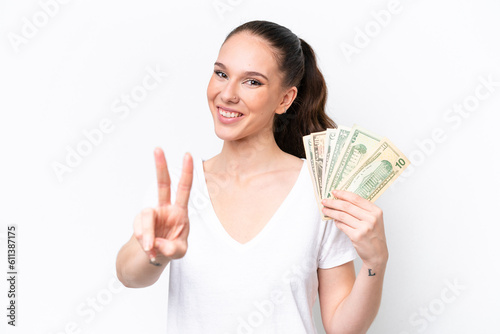 Young caucasian woman taking a lot of money isolated on white background smiling and showing victory sign