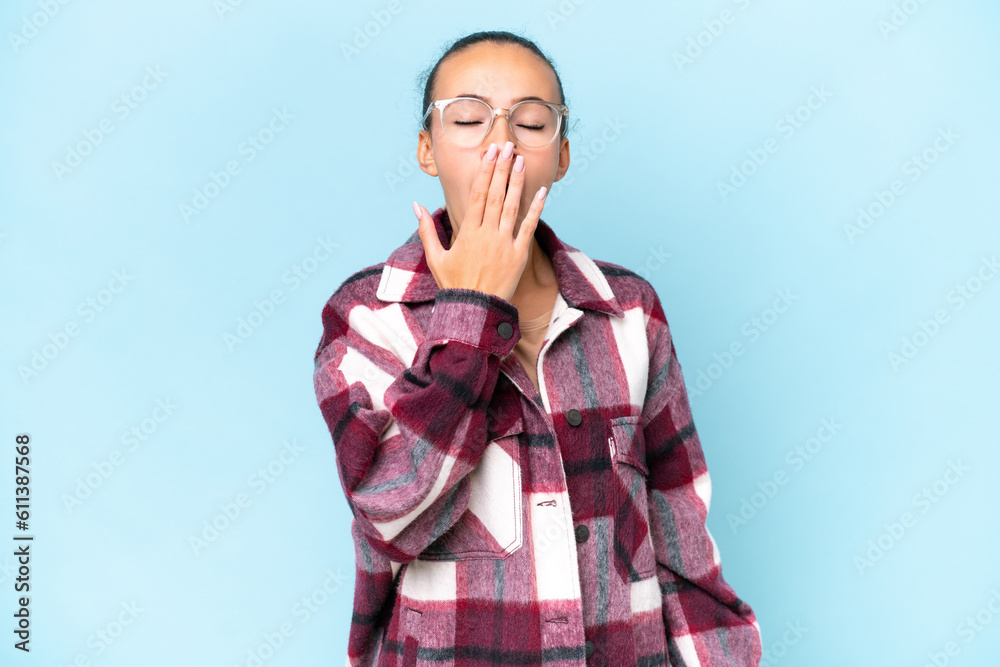 Young Arab woman isolated on blue background yawning and covering wide open mouth with hand Young Arab woman isolated on blue background yawning and covering wide open mouth with hand