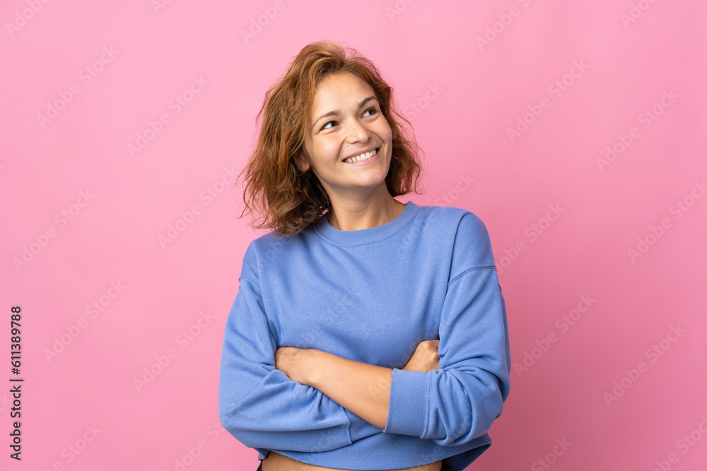 Fototapeta premium Young Georgian woman isolated on pink background looking up while smiling