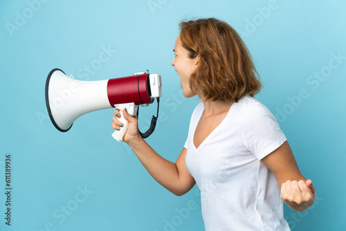 Young Georgian woman isolated on blue background shouting through a megaphone to announce something in lateral position