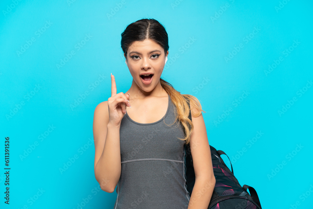 Young sport Russian girl with sport bag isolated on blue background intending to realizes the solution while lifting a finger up Young sport Russian girl with sport bag isolated on blue background intending to realizes the solution while lifting a finger up