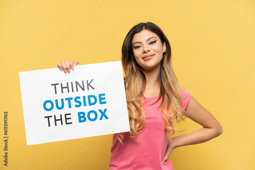 Young Russian girl isolated on yellow background holding a placard with text Think Outside The Box with happy expression Young Russian girl isolated on yellow background holding a placard with text Think Outside The Box with happy expression