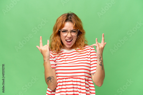 Young caucasian woman isolated on green screen chroma key background making horn gesture