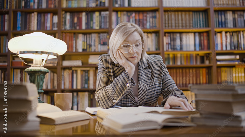 Mature woman tired from overtime work in the library, a journalist studying archives Mature woman tired from overtime work in the library, a journalist studying archives