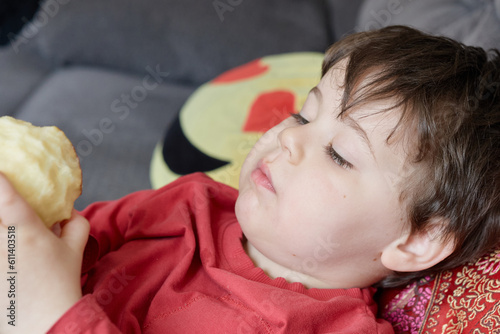 cute expressive young boy lounging on the couch and eating an apple at home photo