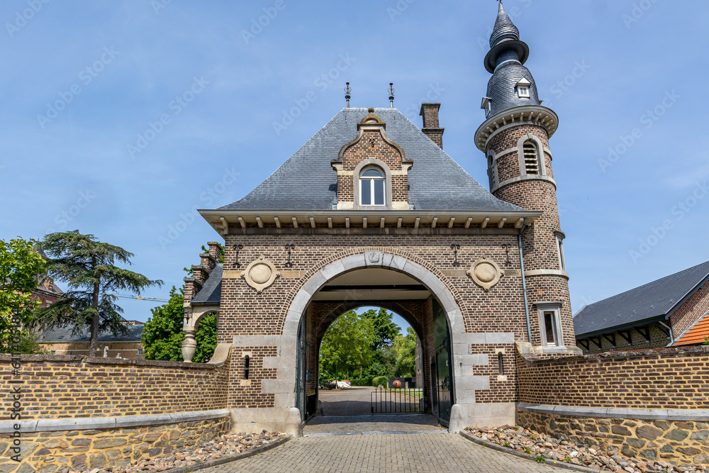 Arched entrance to Borgharen Castle against blue sky, dome with a small window, circular tower, brick walls and fence, trees in background, sunny spring day in South Limburg, Netherlands