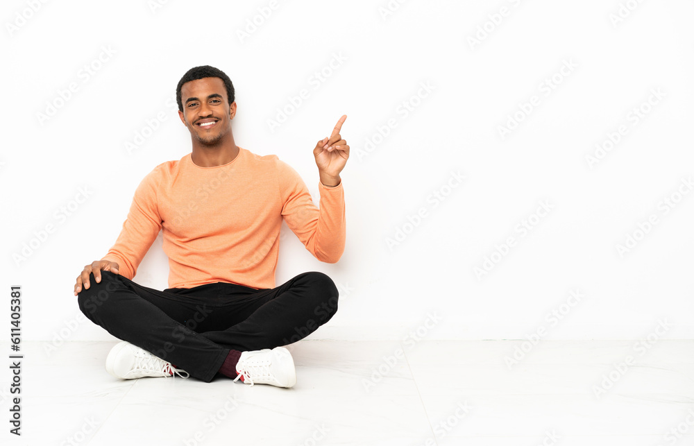 African American man sitting on the floor over isolated copyspace background showing and lifting a finger in sign of the best African American man sitting on the floor over isolated copyspace background showing and lifting a finger in sign of the best
