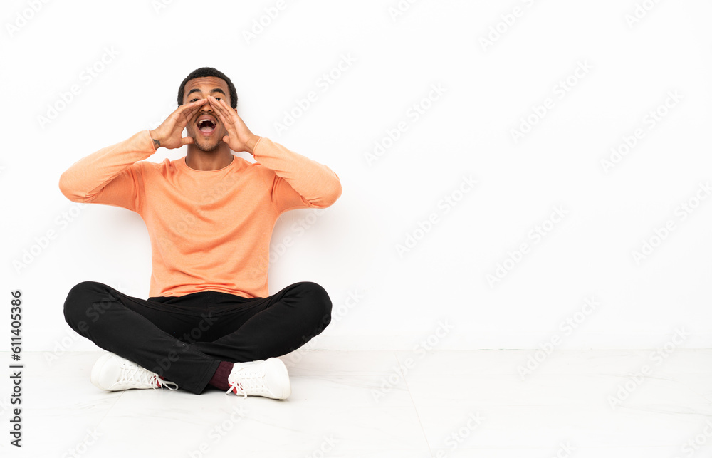 African American man sitting on the floor over isolated copyspace background shouting and announcing something African American man sitting on the floor over isolated copyspace background shouting and announcing something