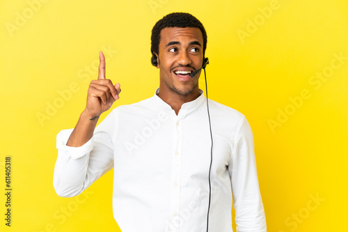African American Telemarketer man working with a headset over isolated yellow background intending to realizes the solution while lifting a finger up