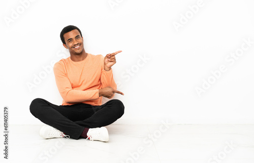African American man sitting on the floor over isolated copyspace background pointing finger to the side and presenting a product