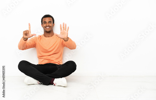 African American man sitting on the floor over isolated copyspace background counting seven with fingers