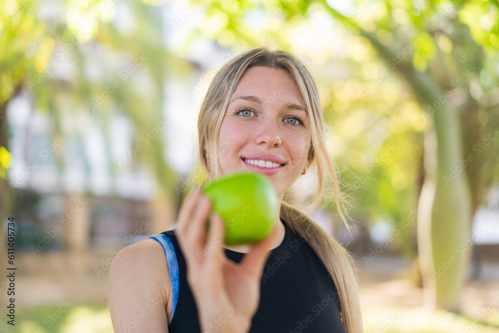 Young blonde woman at outdoors holding an apple with happy expression Young blonde woman at outdoors holding an apple with happy expression