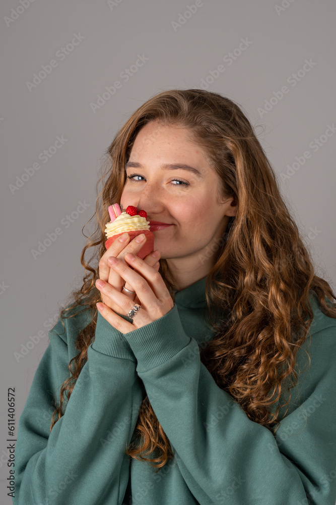 A cute girl is holding a cake-candle. Red-haired happy girl on a gray background A cute girl is holding a cake-candle. Red-haired happy girl on a gray background